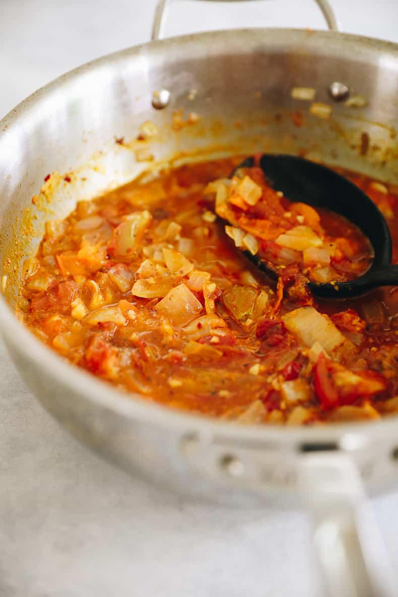 Cooking tomatoes, onions and garlic in a large pot to make homemade arrabbiata sauce.