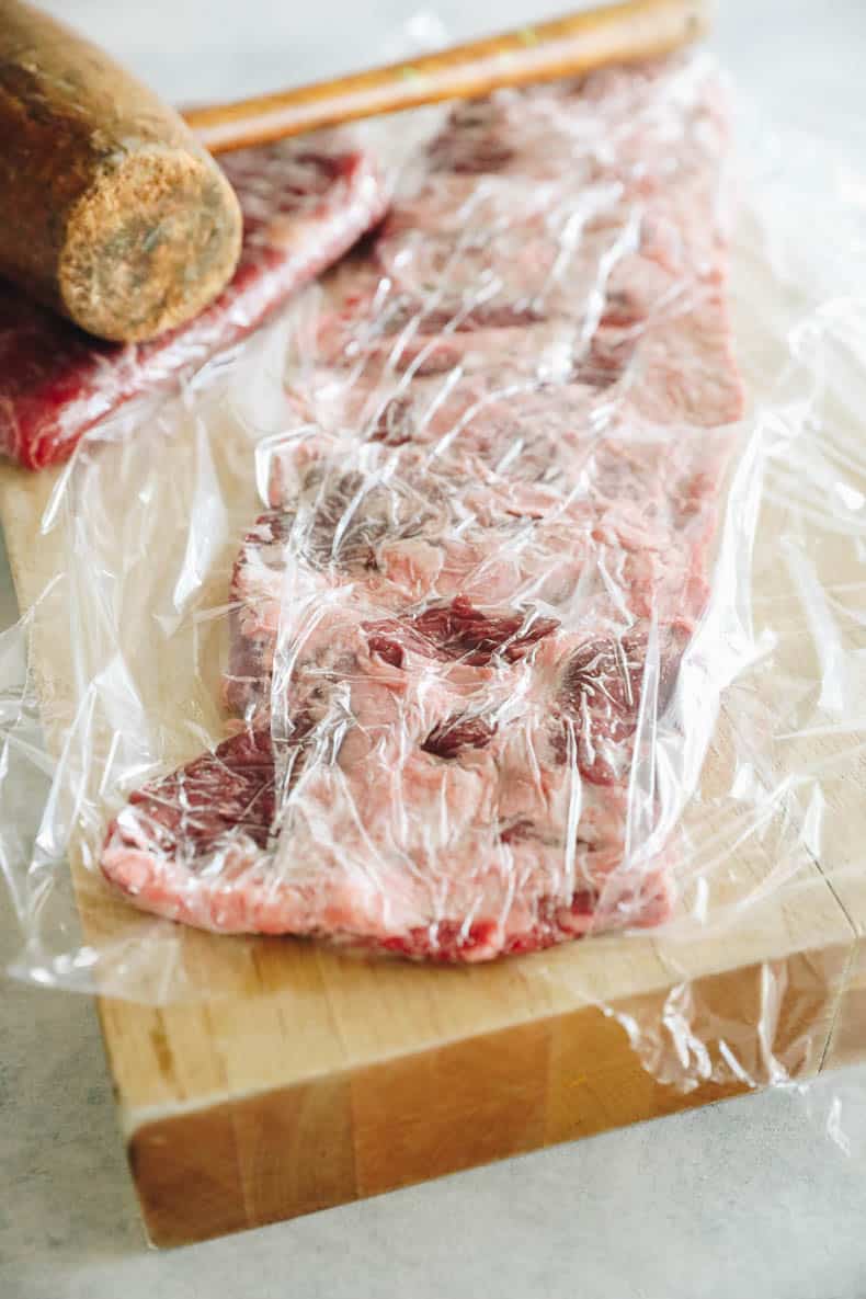 skirt steak covered in plastic wrap and a mallet.