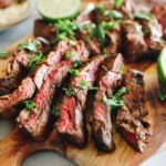 Mexican skirt steak [arrachera] sliced on a brown cutting board with sprinkled cilantro.