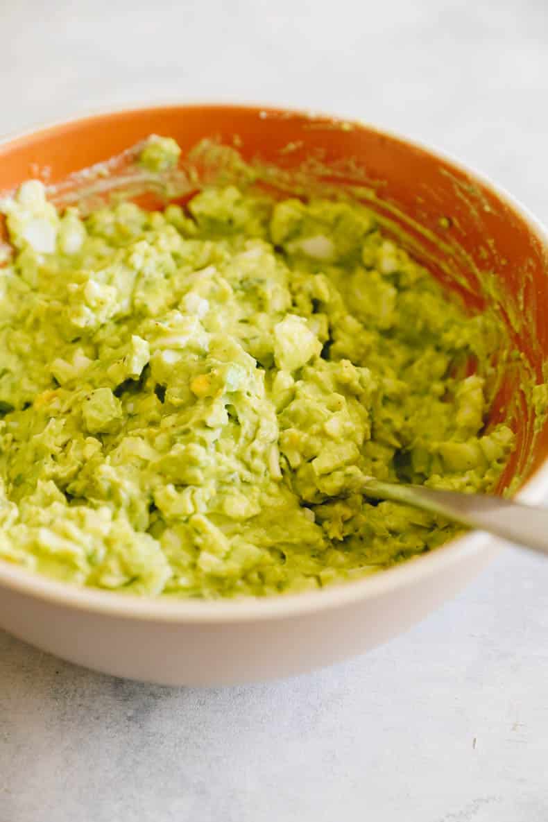 avocado egg salad in a large brown bowl with a spoon.