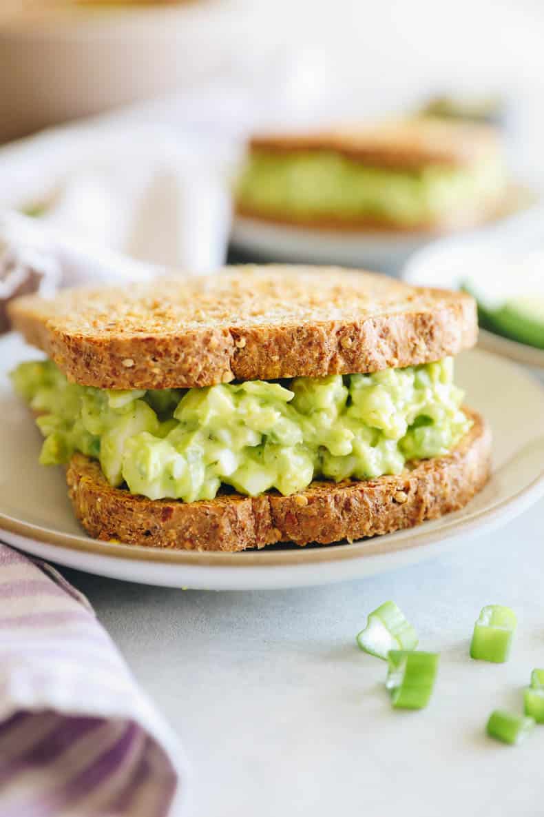 avocado egg salad between two slices of bread on a white plate.