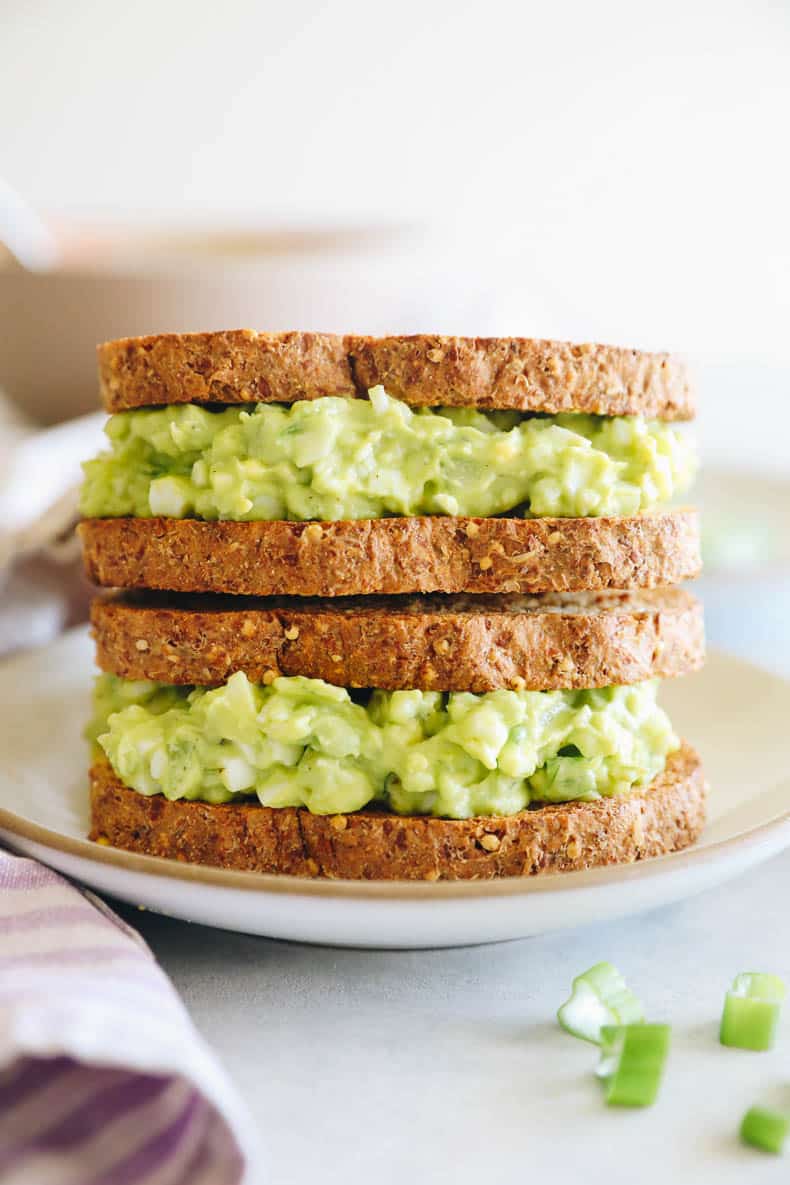 two avocado egg salad sandwiches stacked on top of each other.