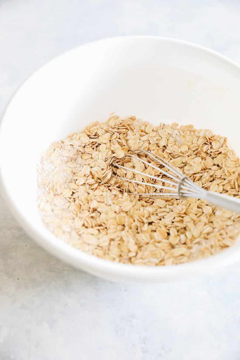 rolled oats, oat flour and cinnamon in a white bowl with a whisk.