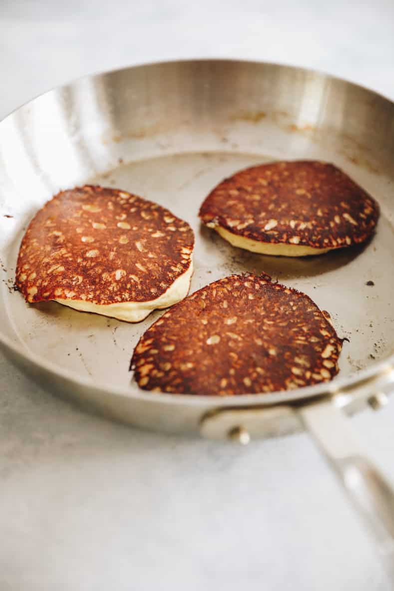 3 banana oatmeal pancakes in silver frying pan.