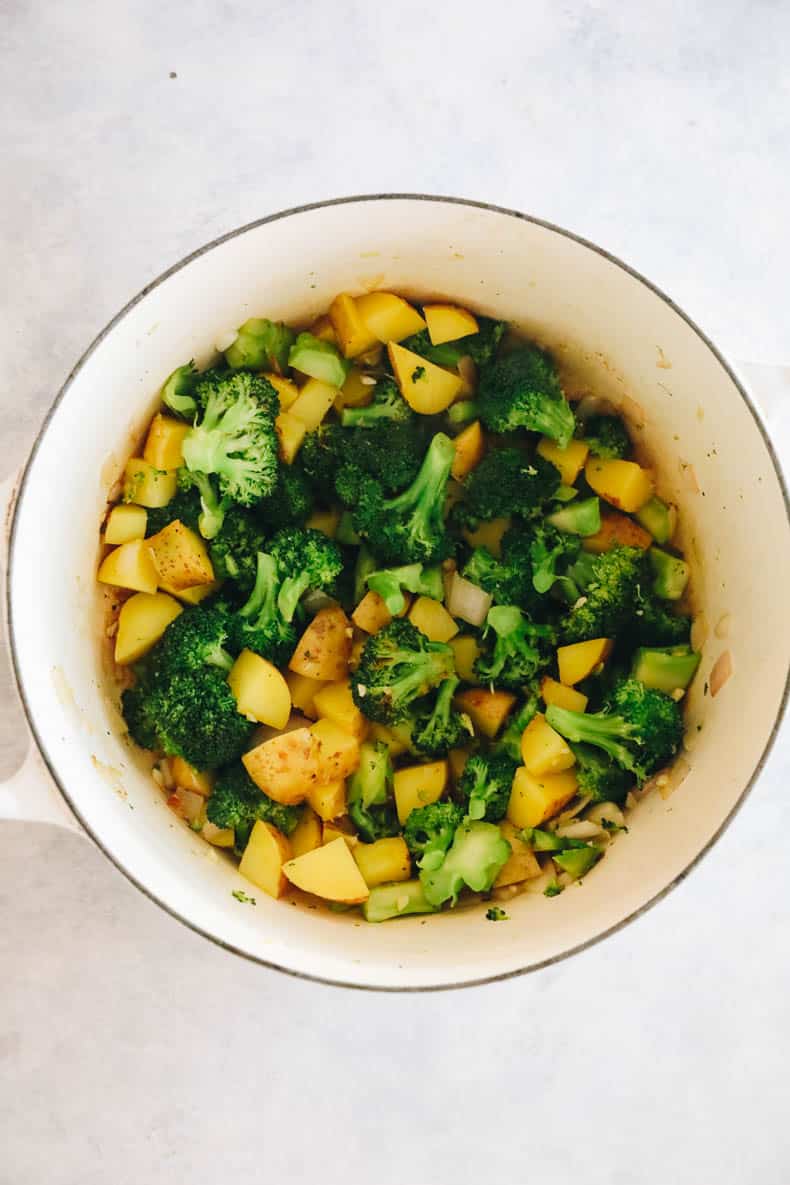 broccoli, potato, shallot and garlic in a large dutch oven being cooked for soup.