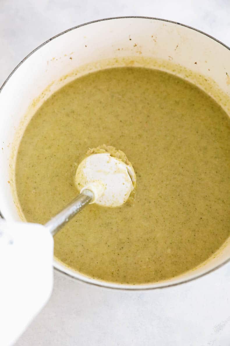 broccoli cheddar soup in a white pot with an immersion blender.