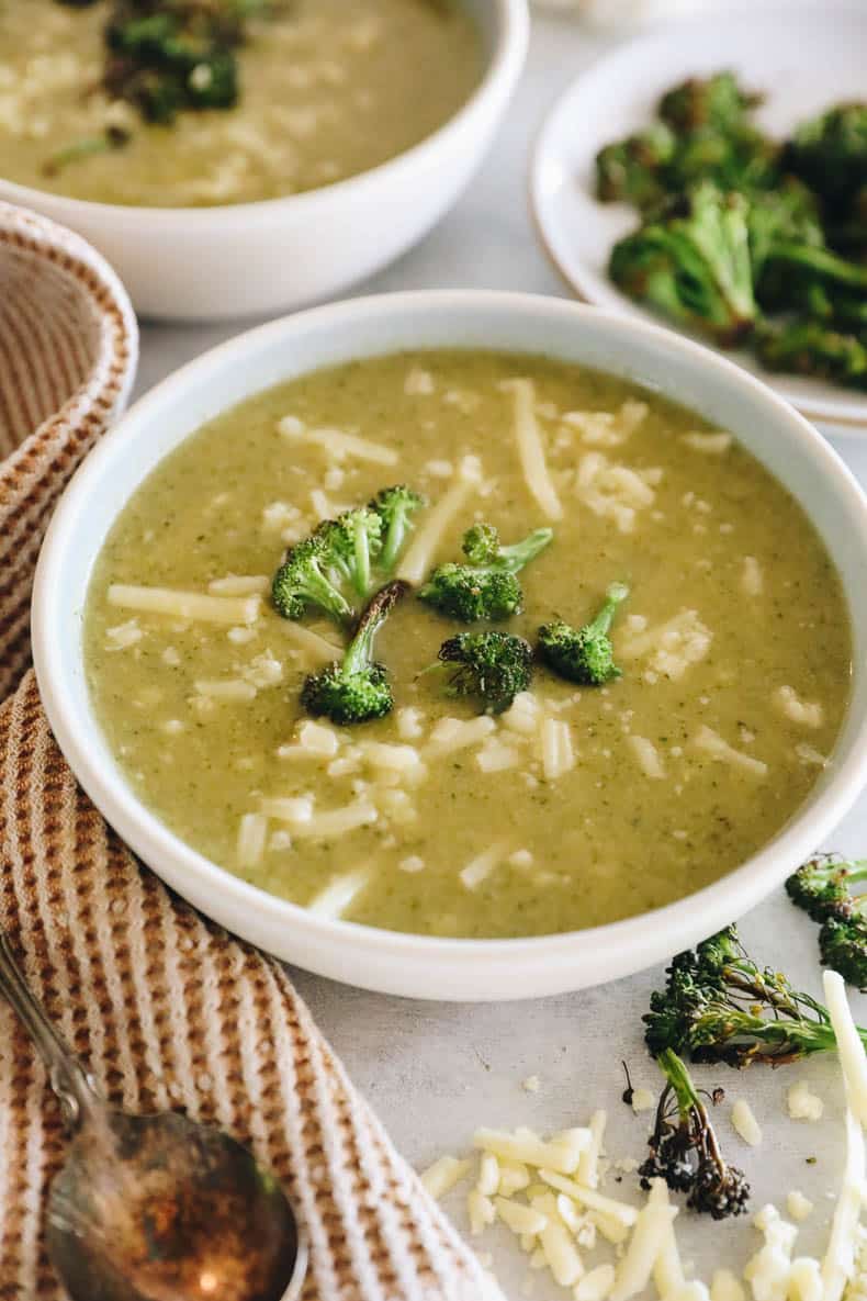 broccoli cheddar soup in a white bowl topped with roasted broccoli and shredded white cheddar