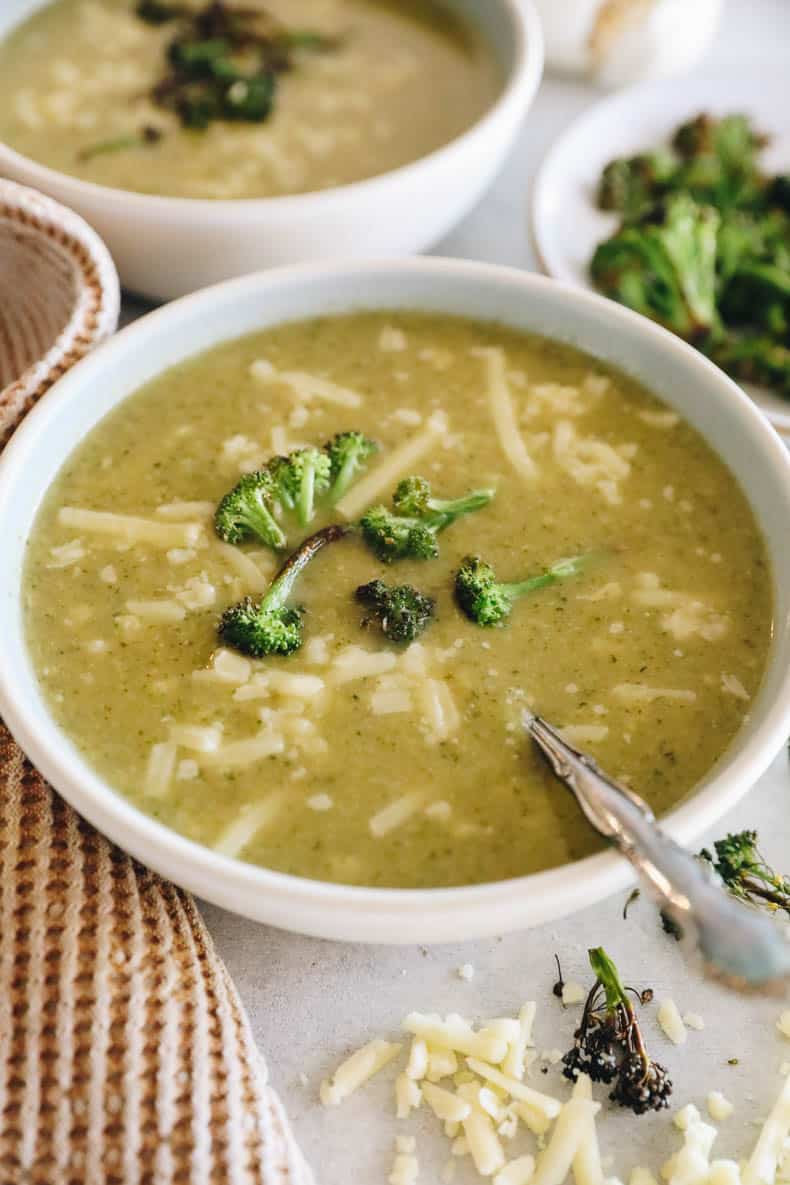 potato broccoli cheddar soup in a white bowl with a spoon and roasted broccoli and shredded white cheddar.