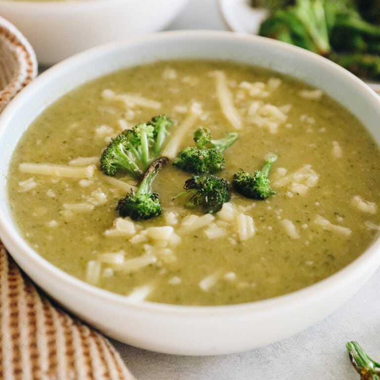 potato broccoli cheddar soup in a white bowl with roasted broccoli and shredded white cheddar cheese.