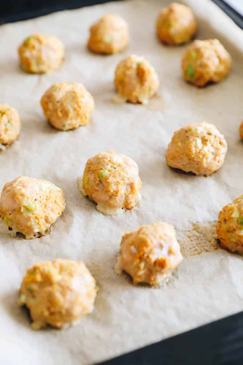 Baked buffalo chicken meatballs on a parchment lined baking sheet.