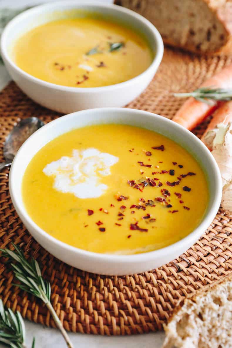 Ginger carrot soup in a white bowl with red pepper flakes and coconut milk.