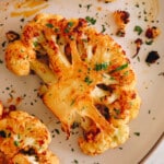 cauliflower steak recipe on a white plate with chopped parsley in an olive oil paprika marinade.