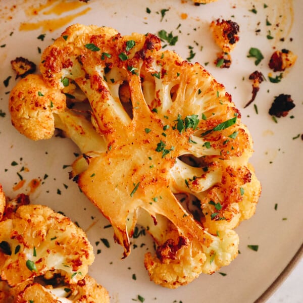 cauliflower steak recipe on a white plate with chopped parsley in an olive oil paprika marinade.