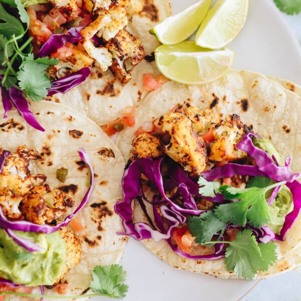 crispy cauliflower tacos on a white plate with cilantro, purple cabbage, guacamole and pico de gallo.