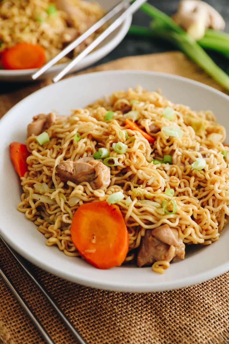 cooked chicken chow mein in a white bowl topped with green onions.