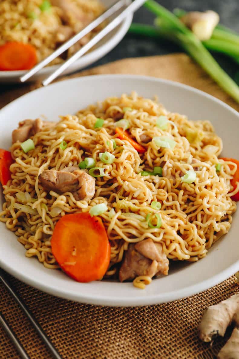 chow mein noodles with chicken carrots, cabbage and green onions in a white plate.