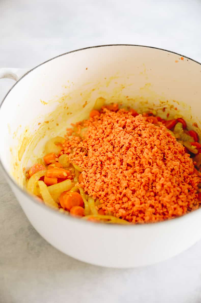 Sautéed vegetables and lentils in a large white pot.