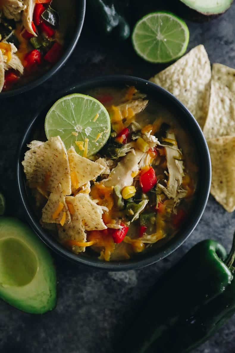 overhead image of chicken poblano soup topped with tortilla chips, cheese and lime juice.