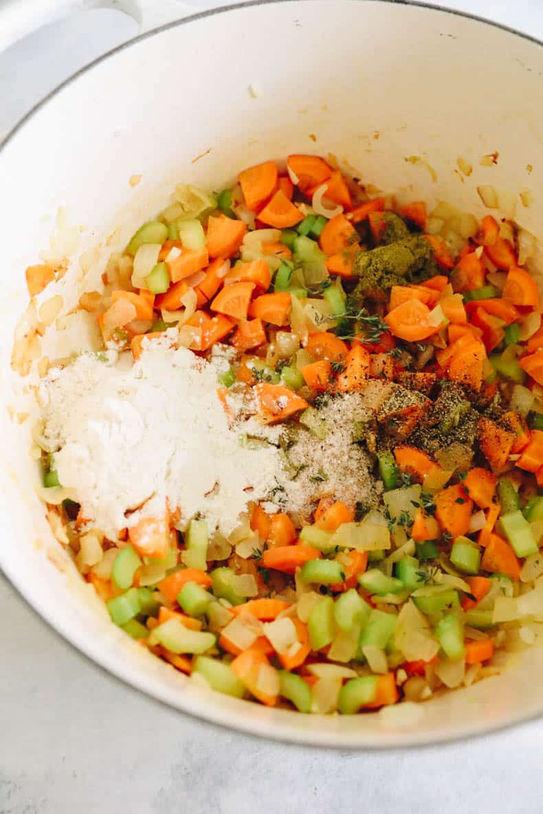 adding spices and flour to a roux in a white dutch oven.