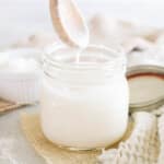 homemade coconut butter in a mason jar with a drippy wooden spoon.