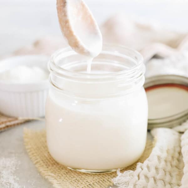 homemade coconut butter in a mason jar with a drippy wooden spoon.