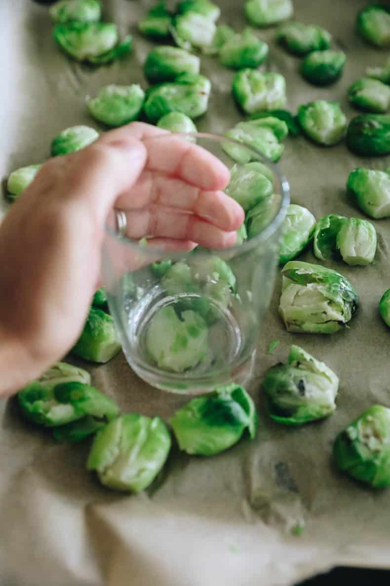 brussel sprouts being smashed with a glass cup on a sheet pan.