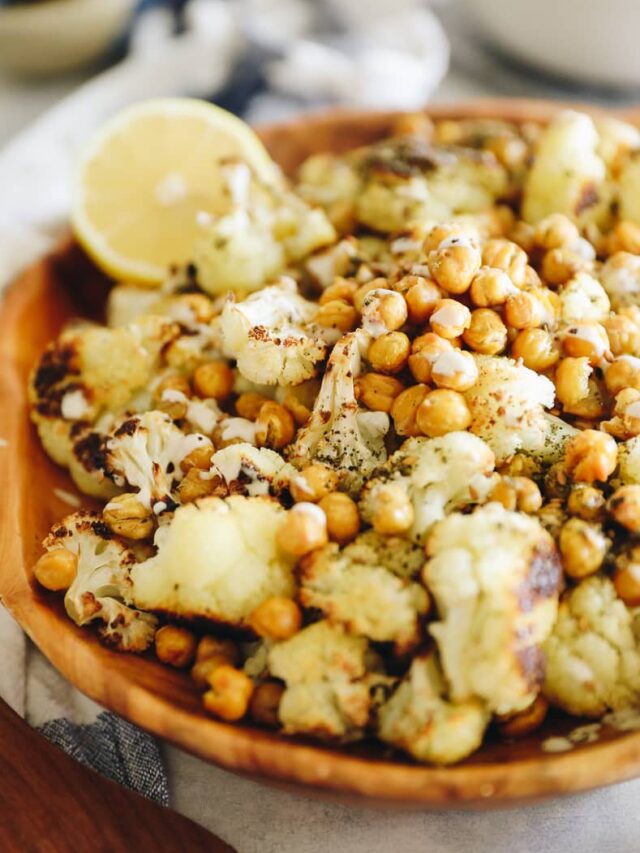 A wooden serving bowl filled with roasted cauliflower and chickpeas.