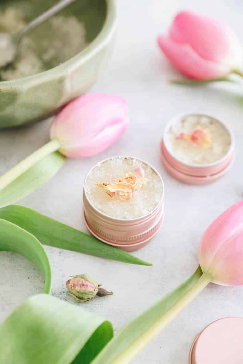 DIY Lip Scrub in a pink metal tin with dried rose petals on top.