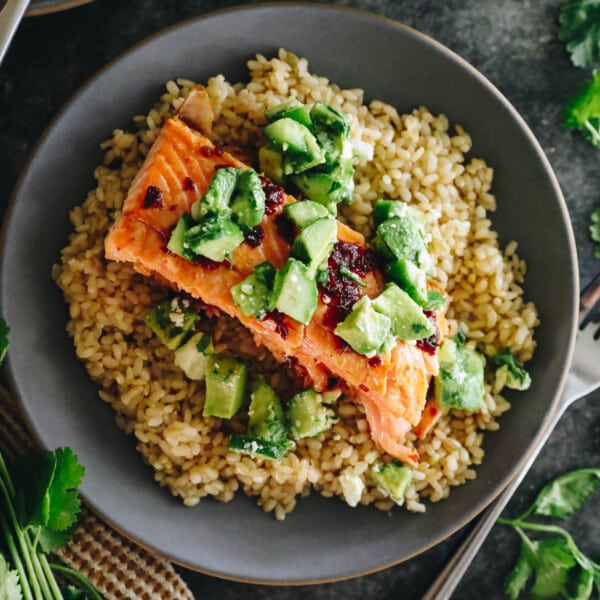 Chipotle baked salmon on a bed of brown rice with an avocado cucumber salsa plated on a blue plate.