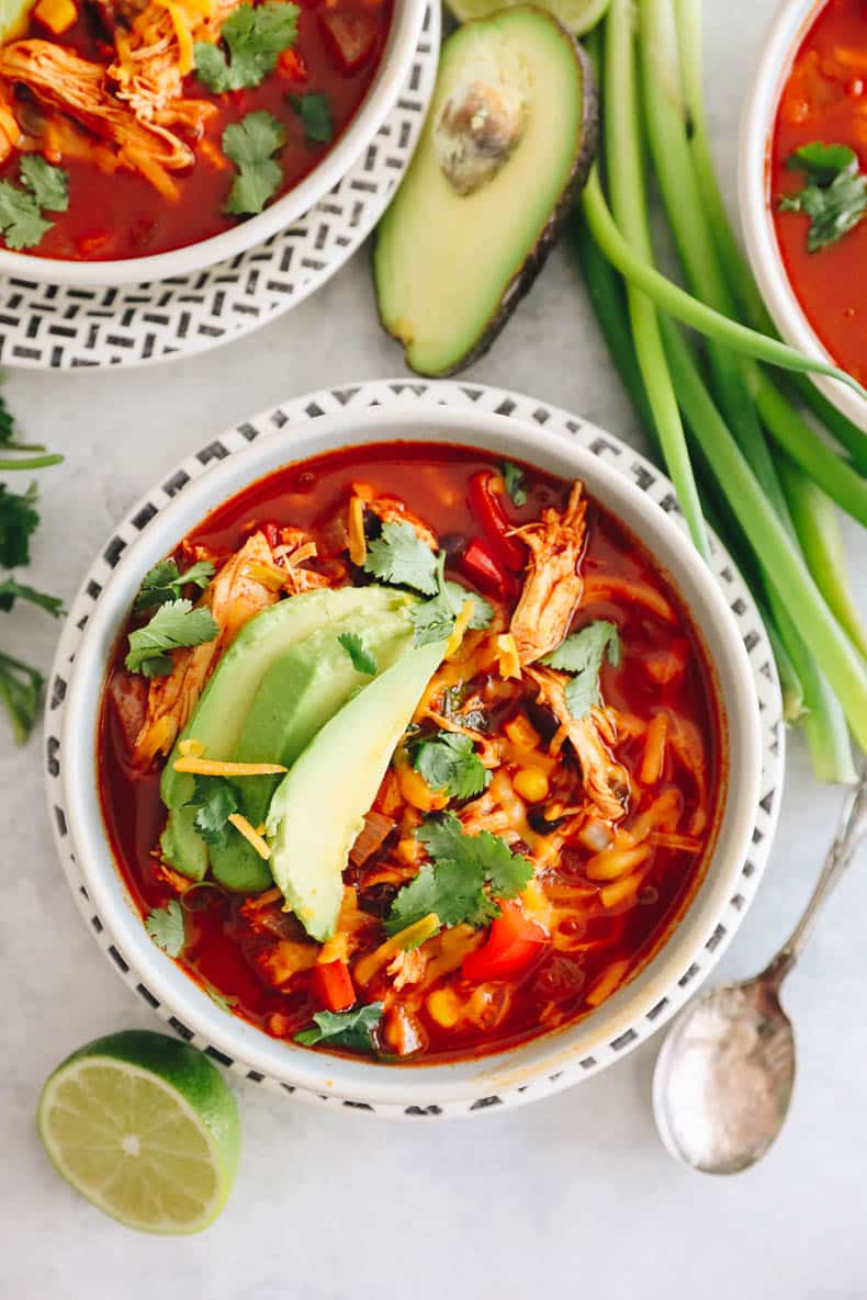 overhead photo of enchilada soup in a white bowl topped with avocado, cheddar and cilantro.