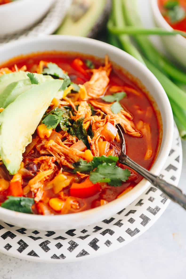 close-up of white bowl with chicken enchilada soup topped with cilantro and avocado.