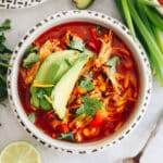 overhead shot of chicken enchilada soup in a white bowl topped with avocado, cheese and cilantro.