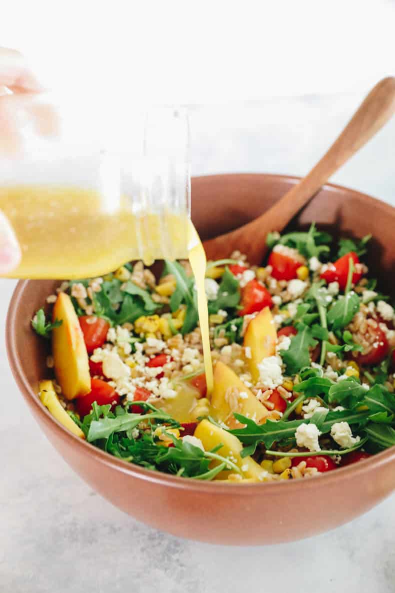 pouring dressing on a farro salad.