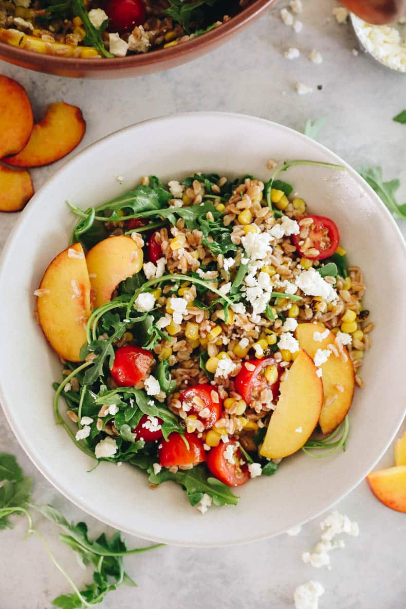 overhead image of a farro salad with peaches, corn, tomatoes and arugula.