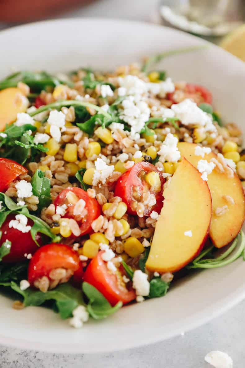 upclose image of a farro salad with feta cheese and arugula, peaches, corn and tomatoes.