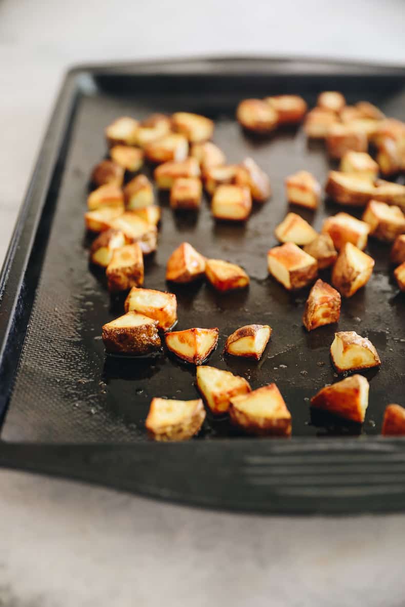 Roasted potatoes for freezer breakfast burritos on a sheet pan with olive oil and salt.