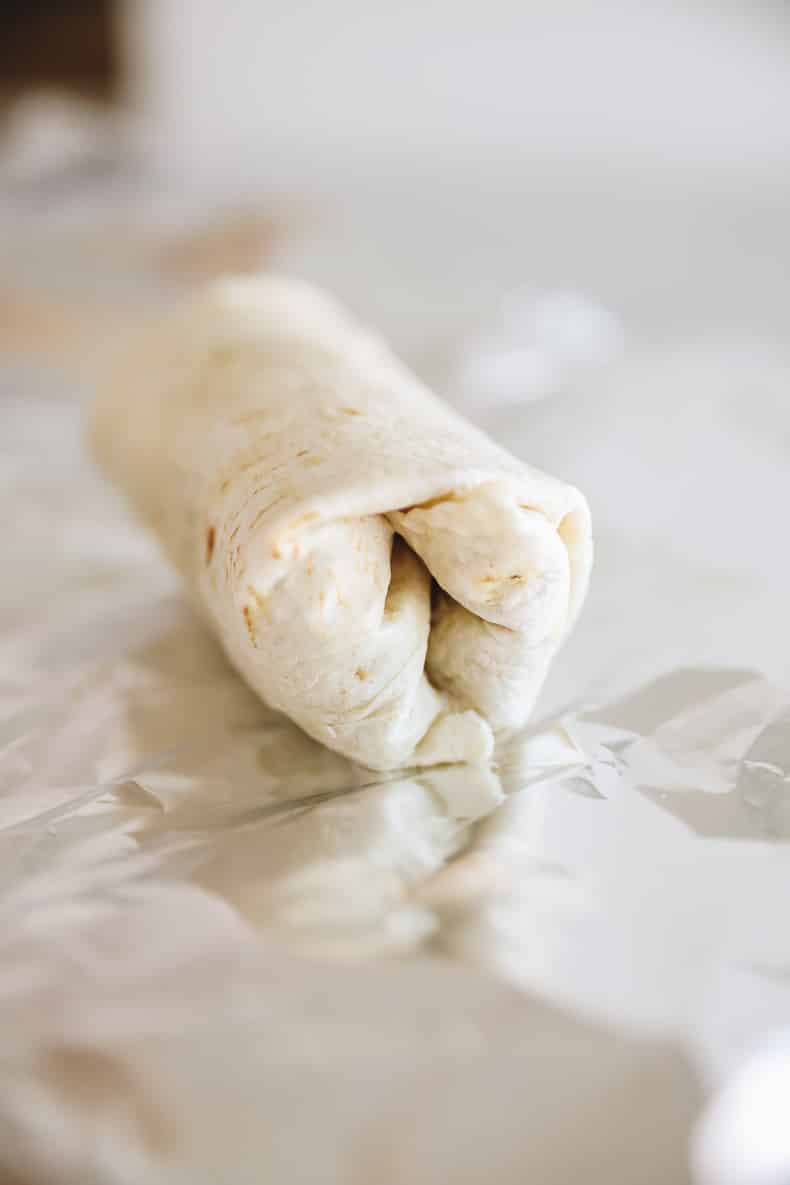 A wrapped up breakfast burrito in a tortilla on a sheet of aluminium foil.