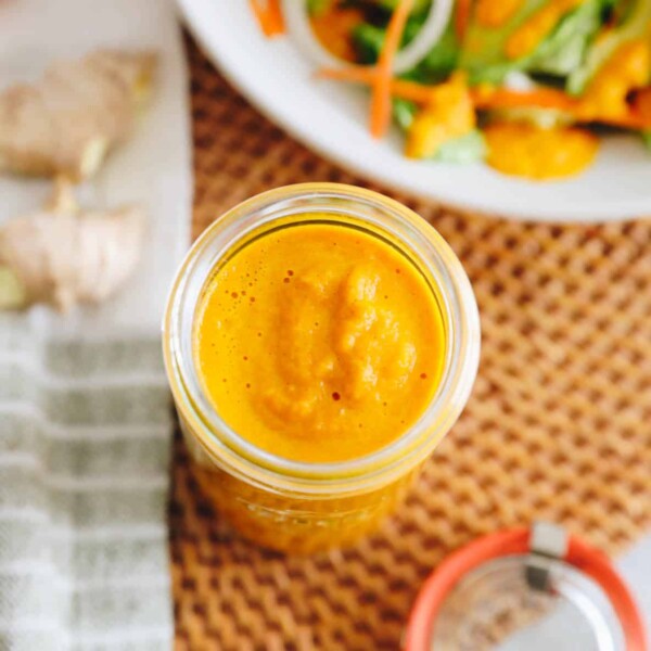 ginger salad dressing stored in a mason jar with a dressed salad in a shallow white bowl.