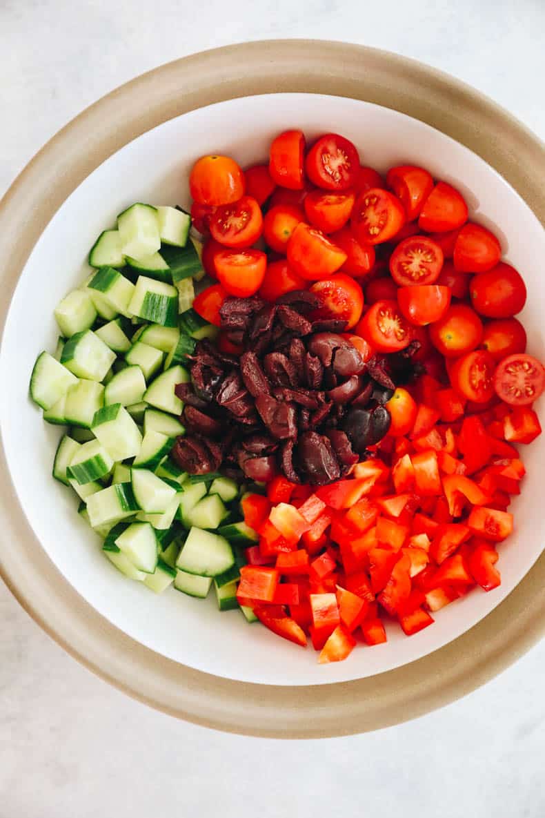 cherry tomatoes, cucumber, olives and bell pepper in a white and brown bowl.