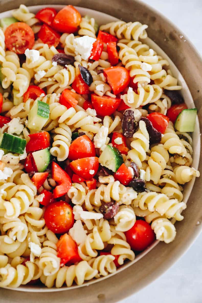 Greek pasta salad in a white and brown bowl.