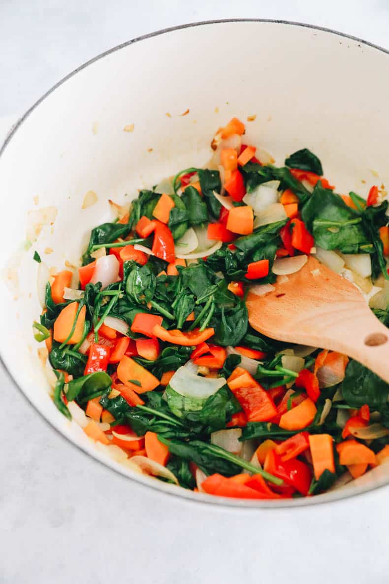 Cooked onion, garlic, carrot, red bell pepper and spinach in a white dutch oven.