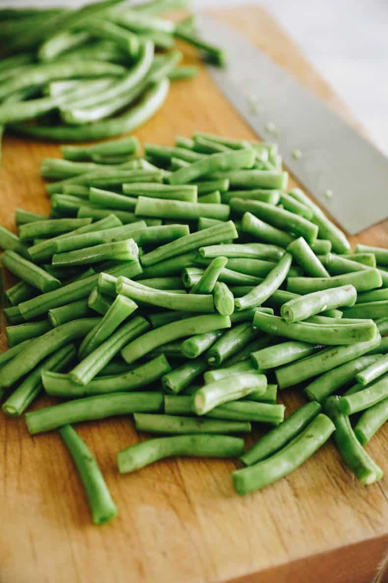 Fresh green beans cut into 1 inch pieces of a cutting board.