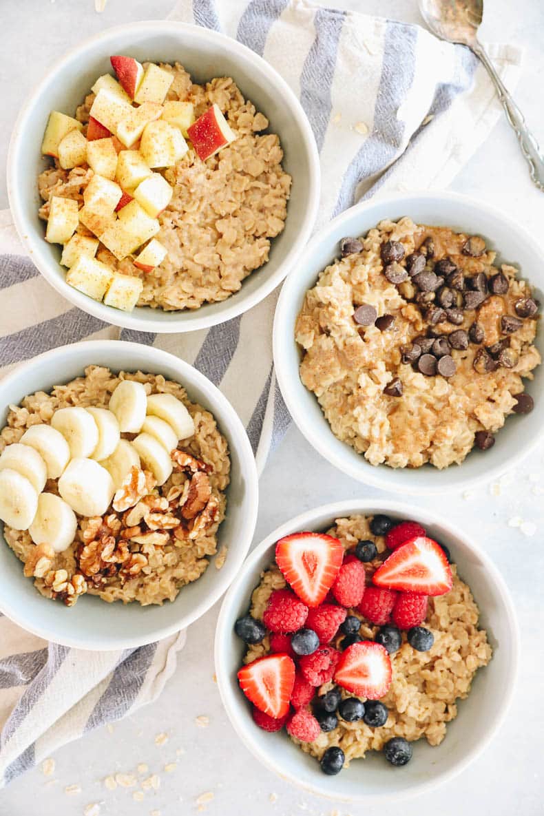 4 bowls of oatmeal topped with different toppings. One with apple cinnamon, one with chocolate peanut butter, one with banana and walnuts and one with raspberries, strawberries and blueberries.