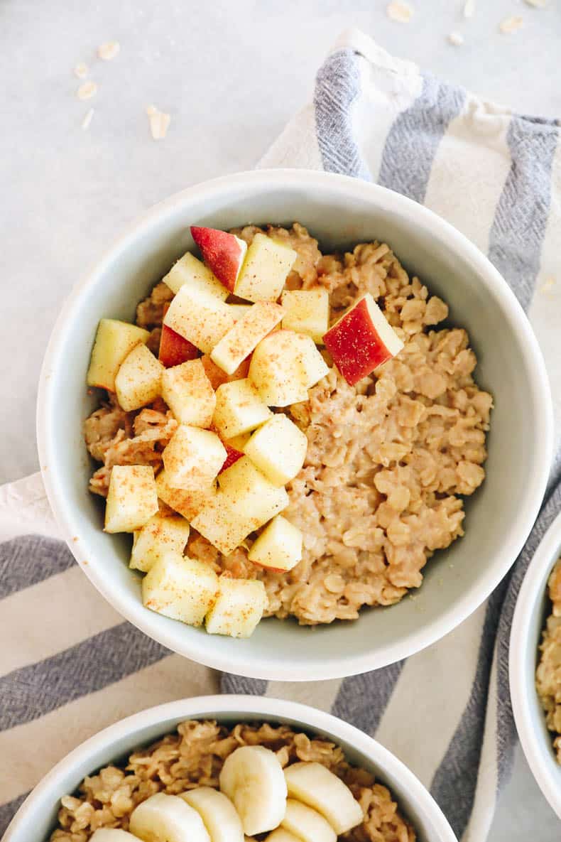 A bowl of oatmeal topped with sliced apple and cinnamon and nutmeg.