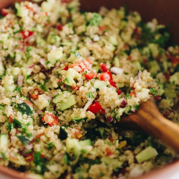 cucumbers, tomatoes, red onion, parsley and white quinoa mixed together in a brown bowl.