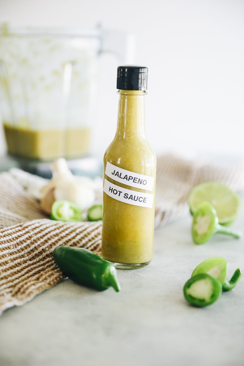 Tall thin hot sauce bottle filled with green jalapeno hot sauce with a label that says "Jalapeno Hot Sauce" in black writing