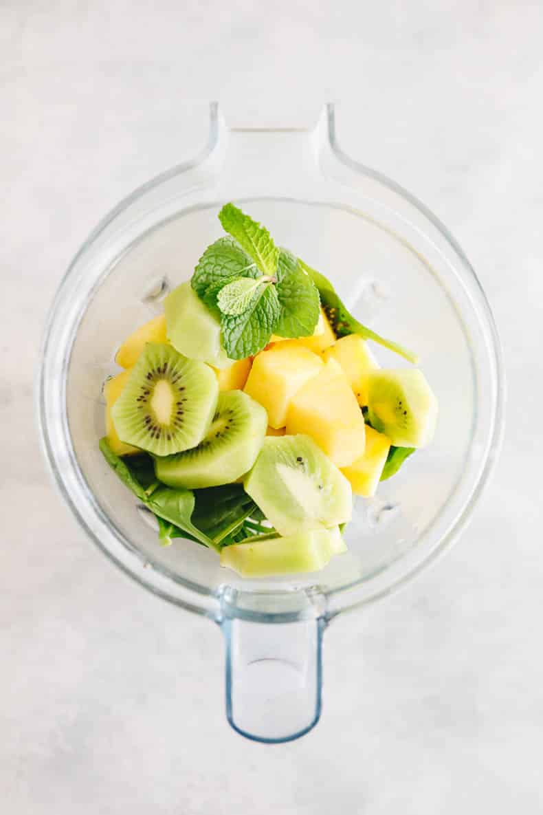 pineapple, kiwi, mint, spinach and other tropical ingredients in a blender.