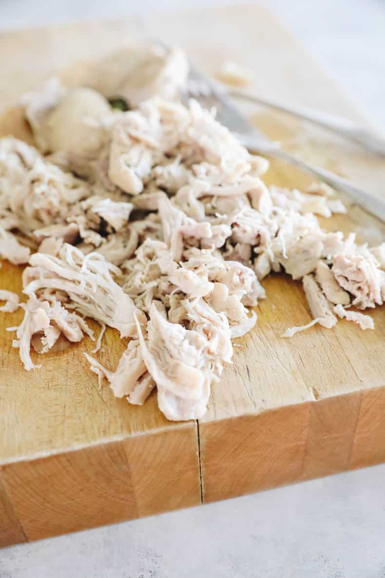 Shredded boneless skinless chicken thighs on a cutting board.