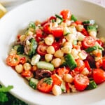 Mediterranean chickpea salad recipe in a white shallow bowl with tomatoes, cucumbers, peppers, parsley and feta.