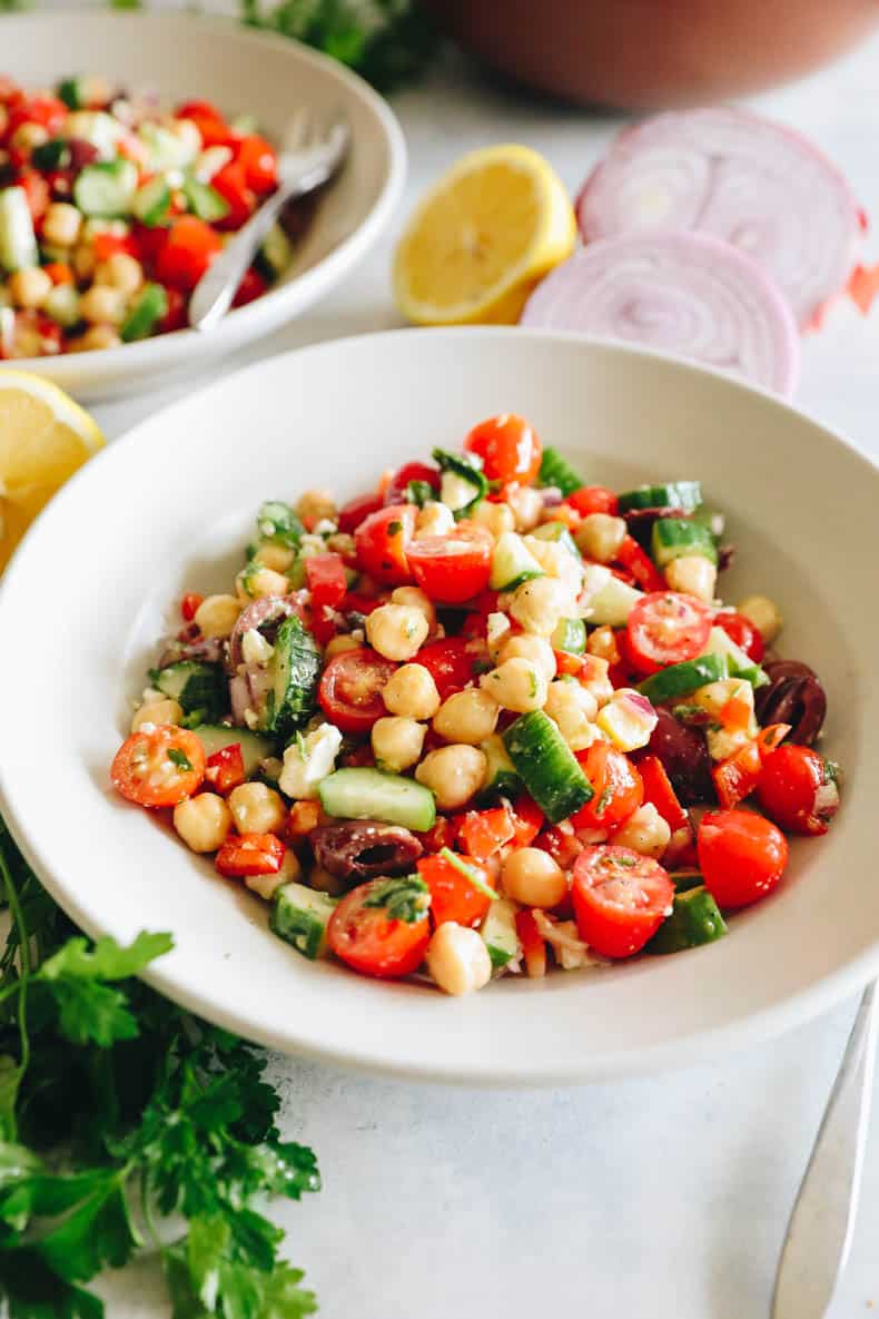 chickpea salad with tomatoes, cucumbers, olives and feta in a white bowl.